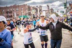 Rick giving high fives to Project Purple runners Elli & Dino on the NYCM course.